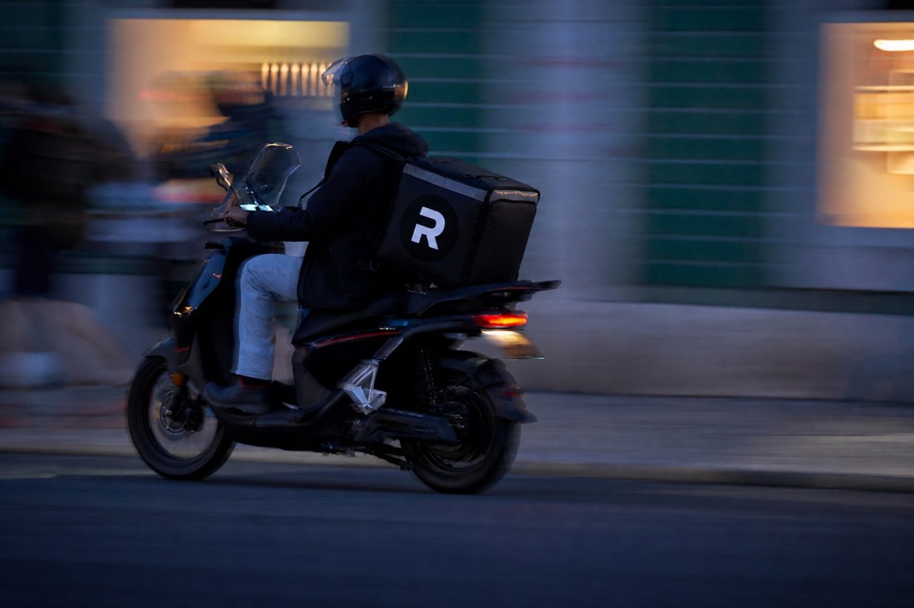 Courier on a scooter at dusk with a black Ryde delivery backpack